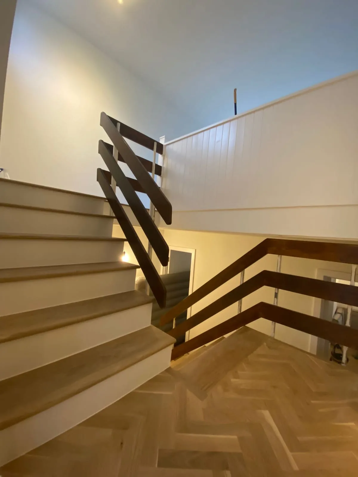 Open-tread oak staircase and dark timber balustrade above a herringbone floor